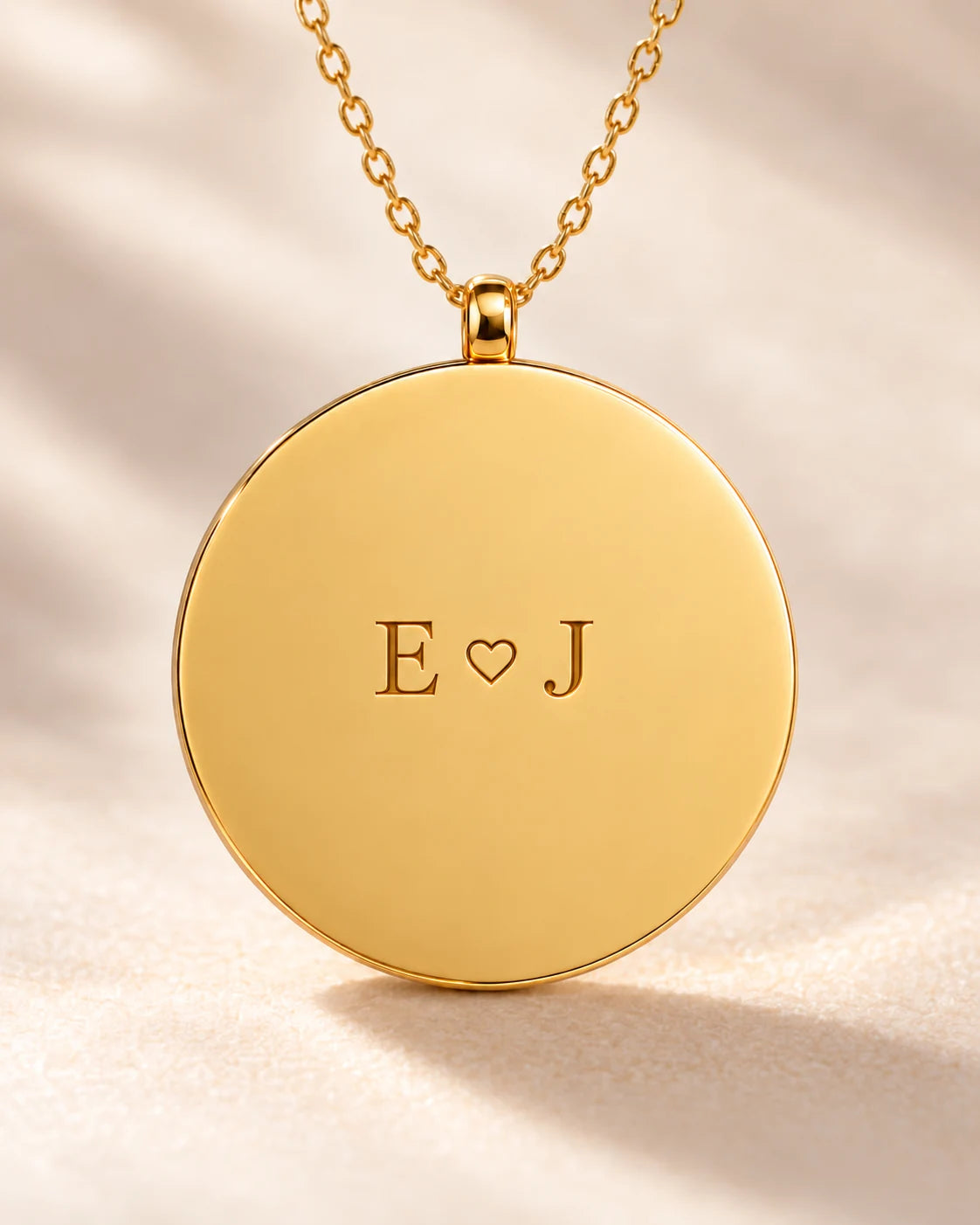 Close-up of the gold pendant front, engraved E heart J